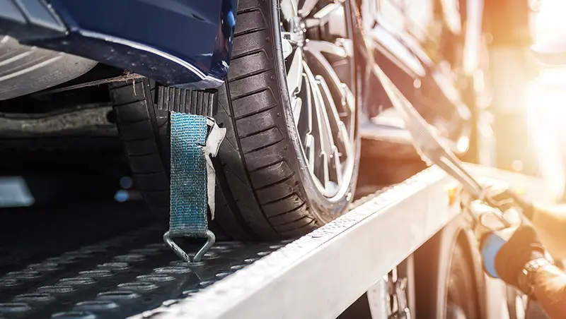 Närbild på personbilsdäck, som är lastad på att bärgningsflak och lastsäkras med spännband